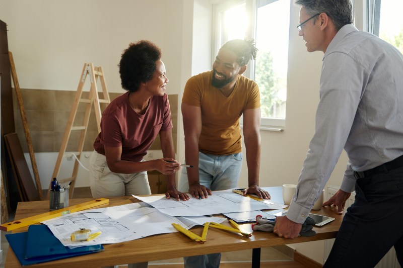 Couple talking while examining blueprints with a building contractor in their apartment