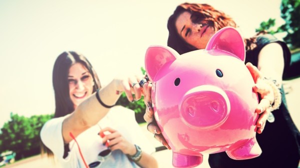 Two young funny woman holding piggy bank in hands, selective focus, outdoors