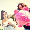 Two young funny woman holding piggy bank in hands, selective focus, outdoors