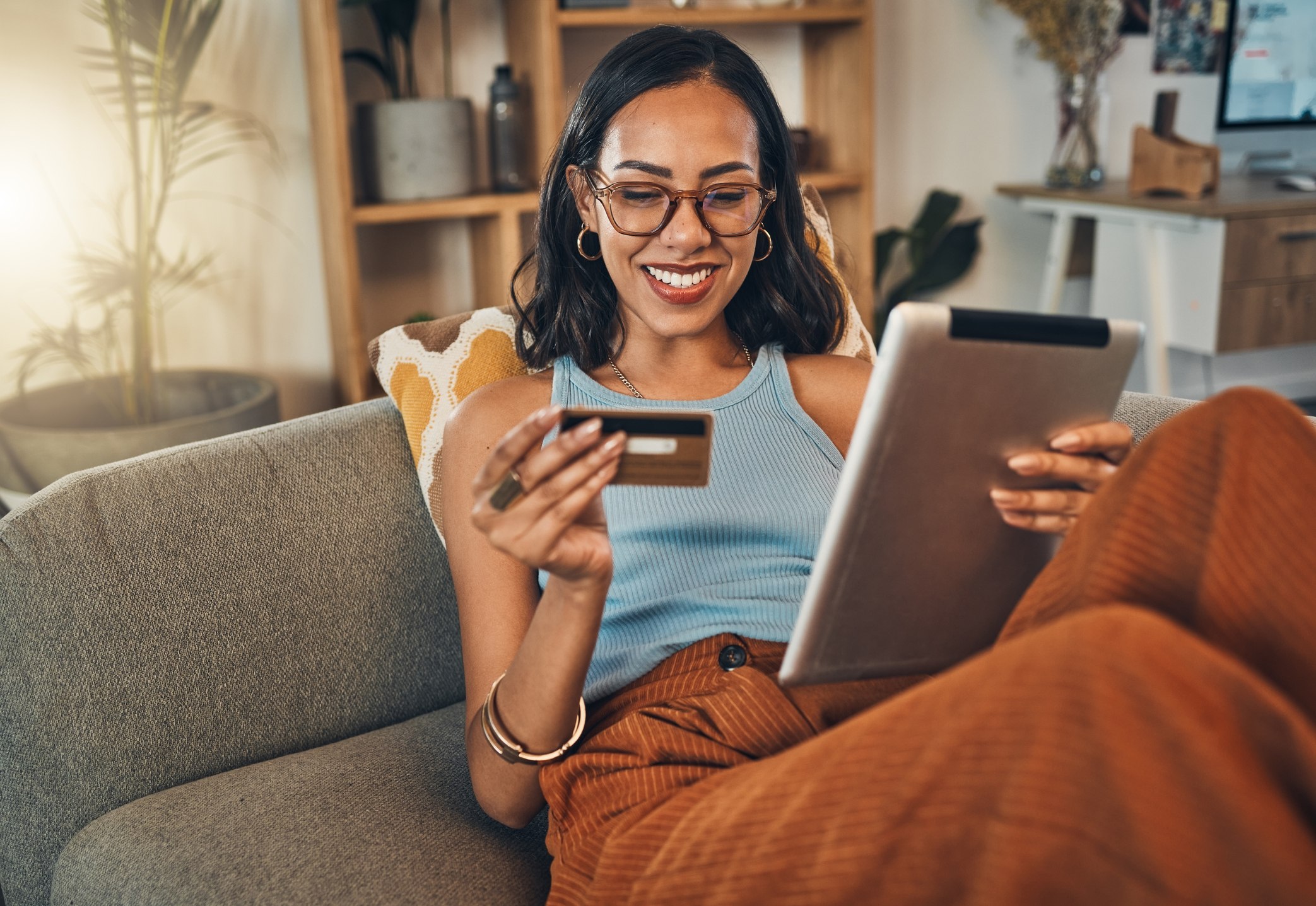 Smiling woman using a credit card while shopping on a digital tablet at home