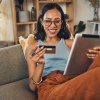 Smiling woman using a credit card while shopping on a digital tablet at home