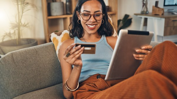 Smiling woman using a credit card while shopping on a digital tablet at home