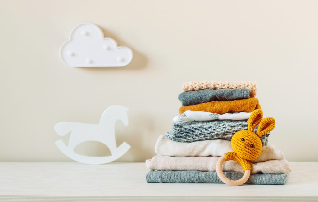 Stack of baby clothes with a rattler toy
