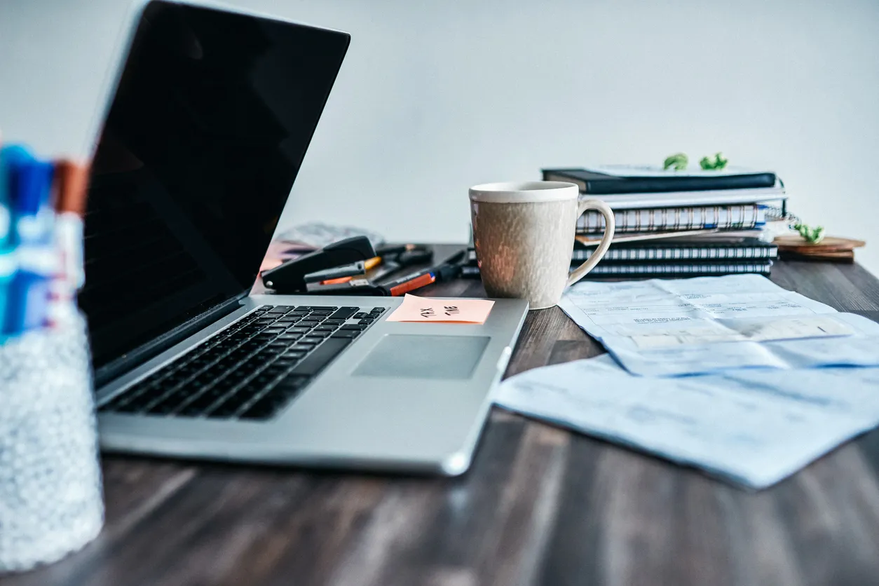 laptop on a desk with papers, coffee mug ad other desk accessories