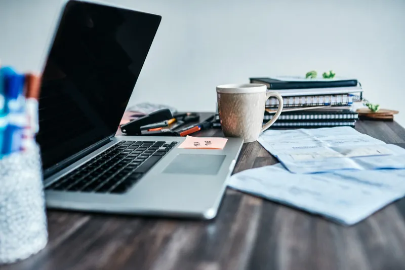 laptop on a desk with papers, coffee mug ad other desk accessories