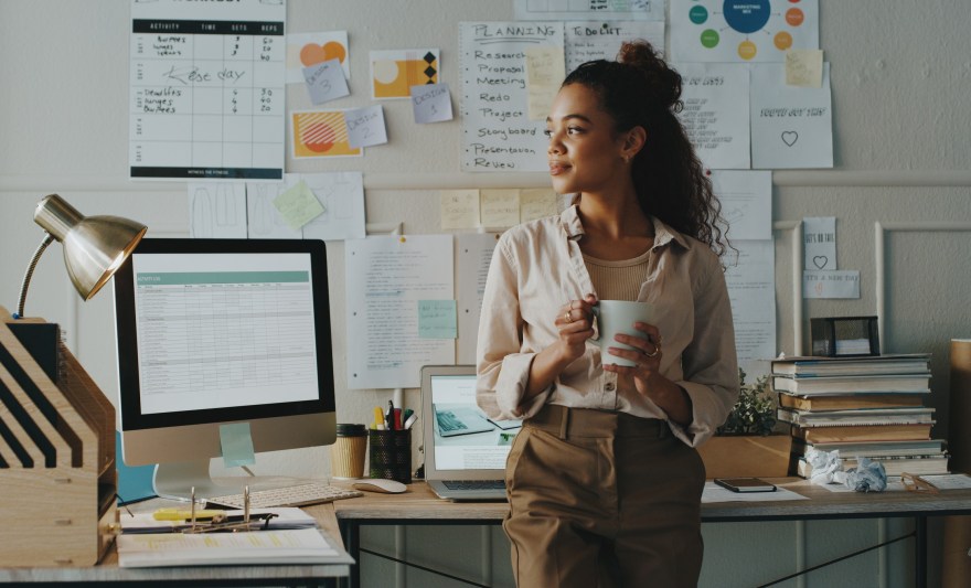  young woman standing and looking contemplative while holding a cup of coffee in her home office