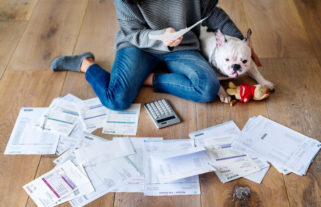 Woman managing the debt while sitting on the floor with her dog and a pile of bills