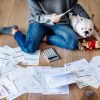 Woman managing the debt while sitting on the floor with her dog and a pile of bills