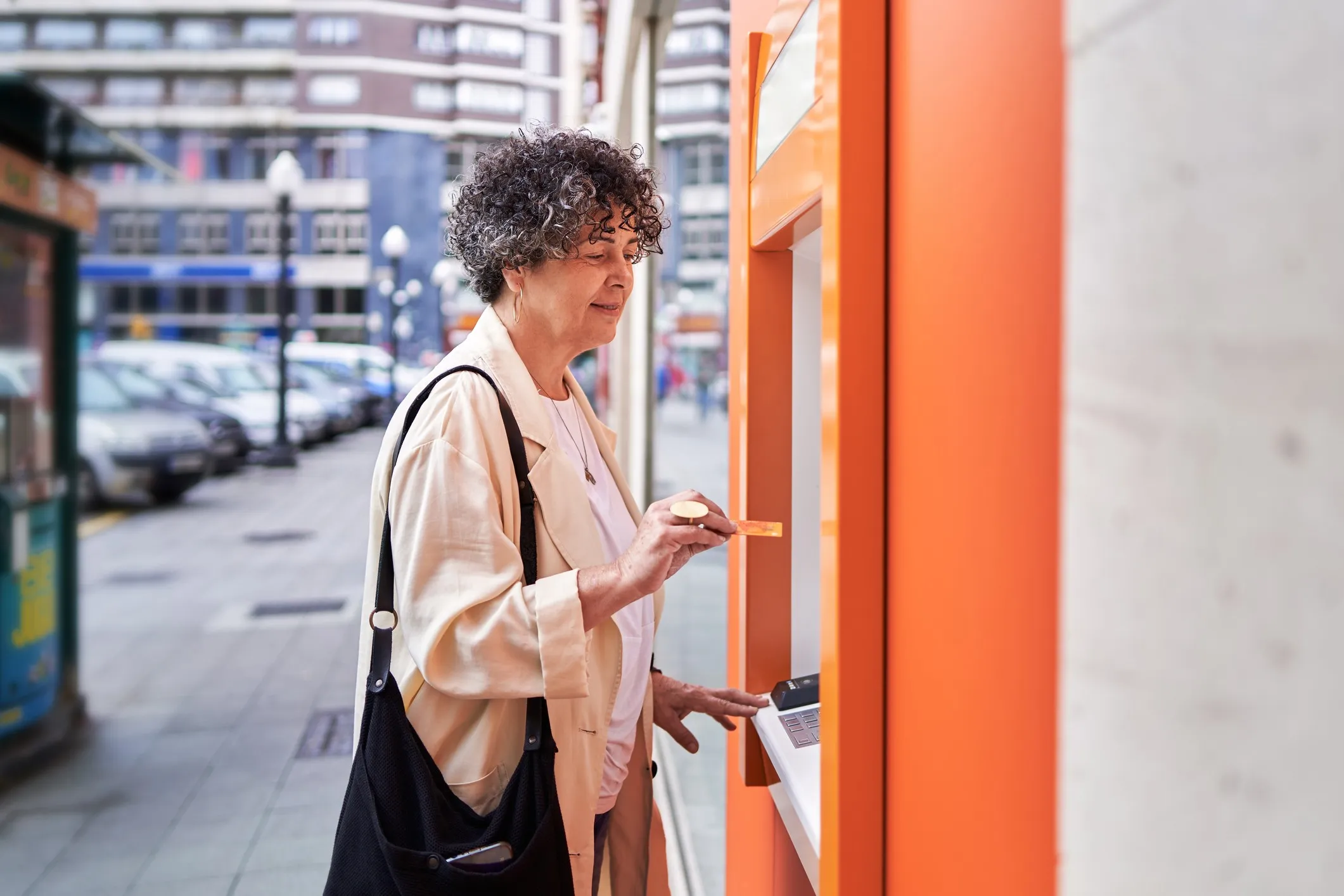 An older woman inserting her credit card into an ATM on a city street
