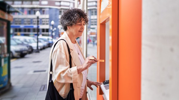 An older woman inserting her credit card into an ATM on a city street