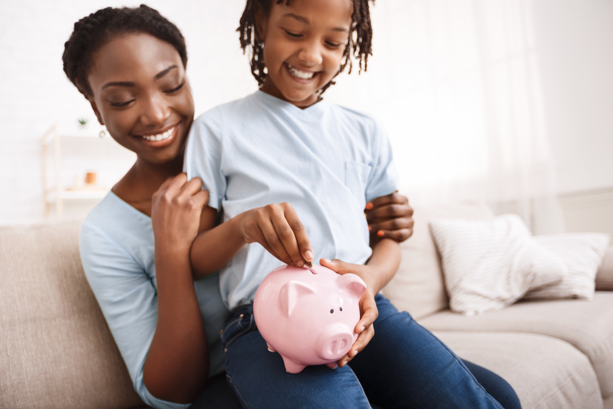 Mother and daughter practicing responsible money habits by depositing coins in a piggy bank