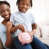 Mother and daughter practicing responsible money habits by depositing coins in a piggy bank