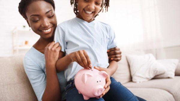 Mother and daughter practicing responsible money habits by depositing coins in a piggy bank