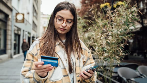 A college student holding her credit card and using a smartphone while walking in the city