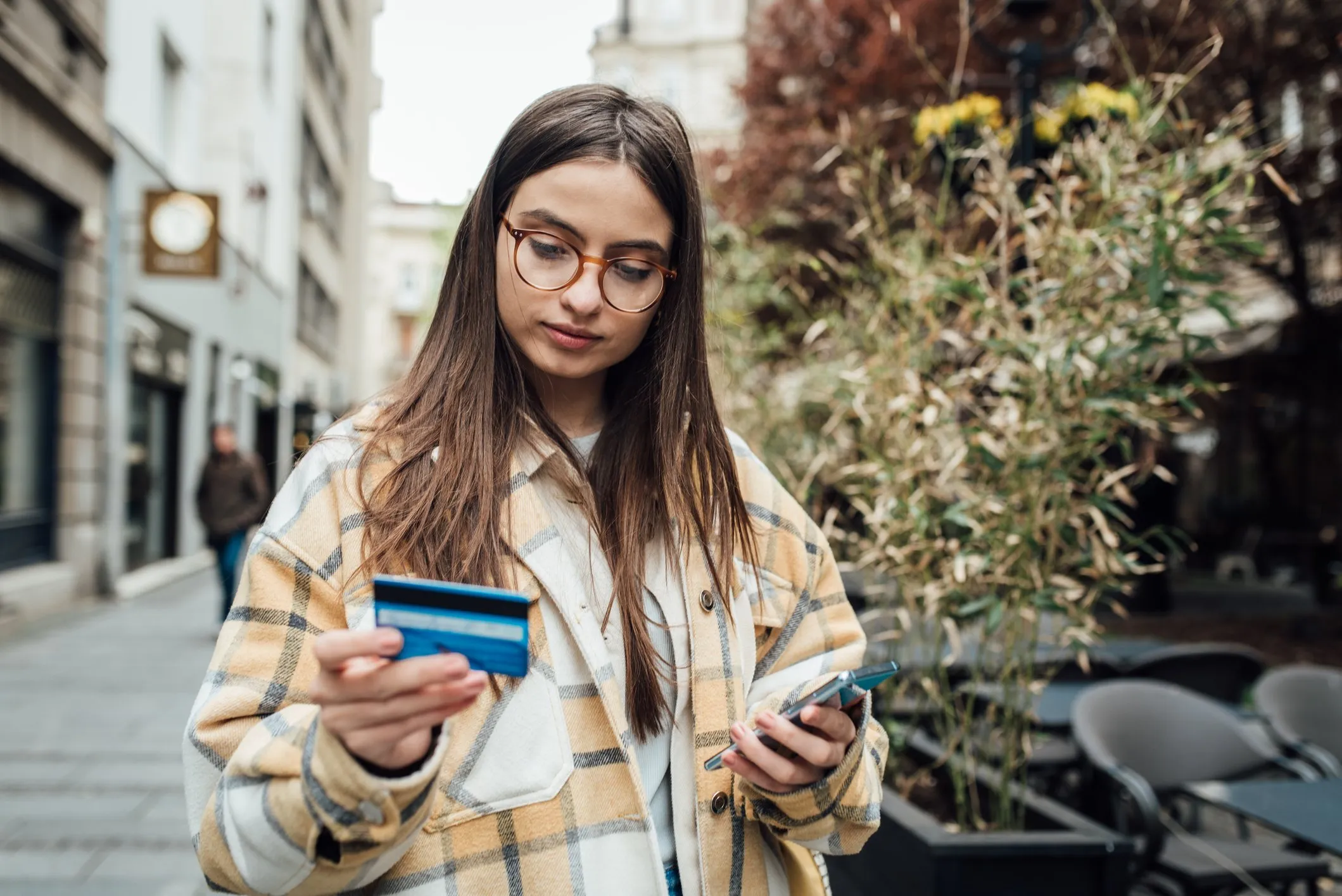 A college student holding her credit card and using a smartphone while walking in the city