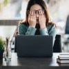 stressed out woman with hands in her face while sitting at her desk