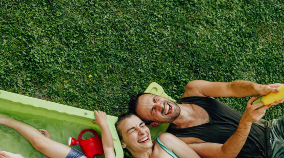 family laughing with their eyes closed while they lie on a lawn