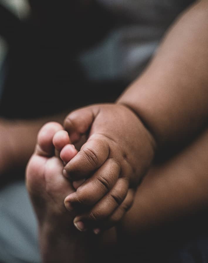 Baby hand holding baby's foot.