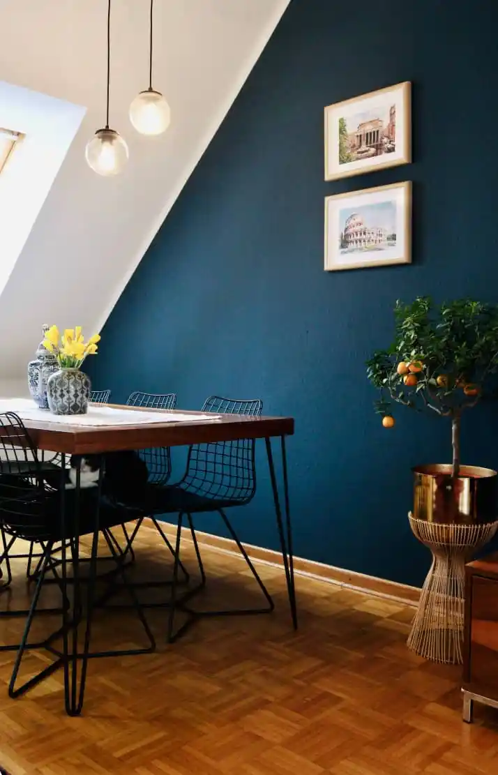 Dining table with flowers in front of a dark blue wall with framed pictures
