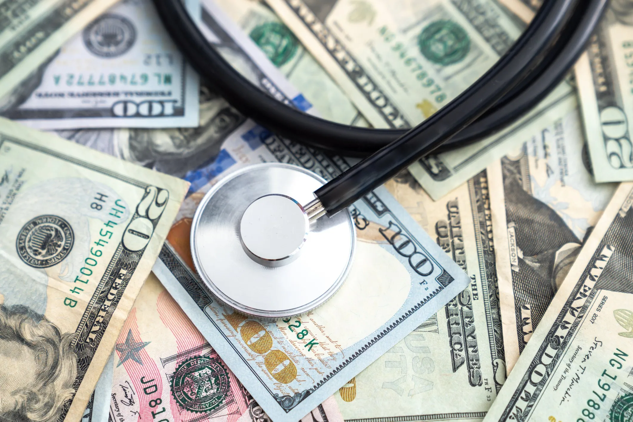 Stethoscope on top of a pile of united states cash covering the entire surface