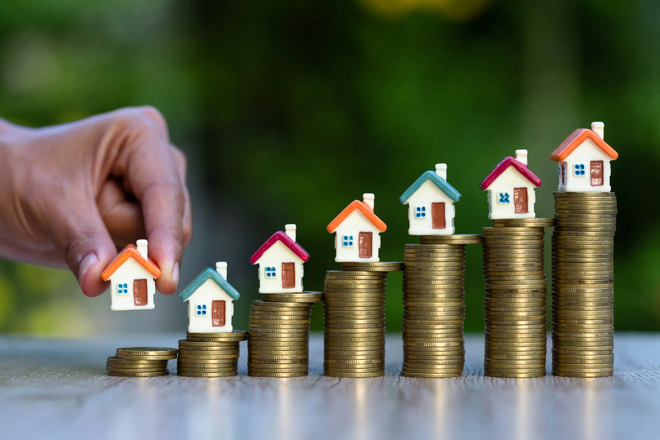 A hand holds a home model to put on a stack coin with other house models with coin stacks