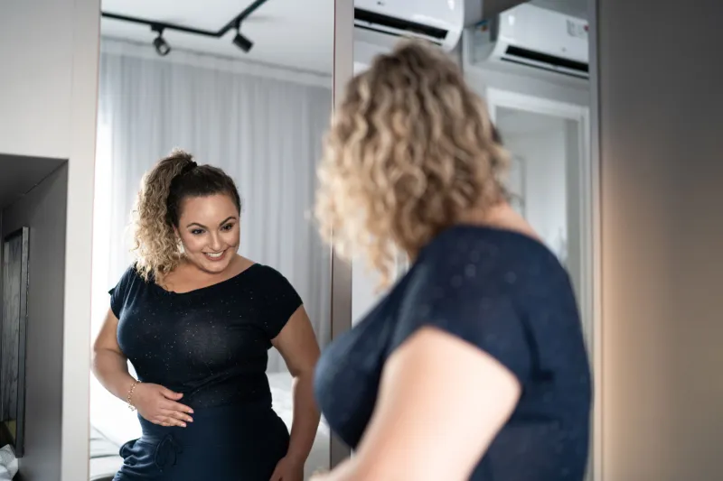 Pretty woman getting dressed in front of a mirror at home