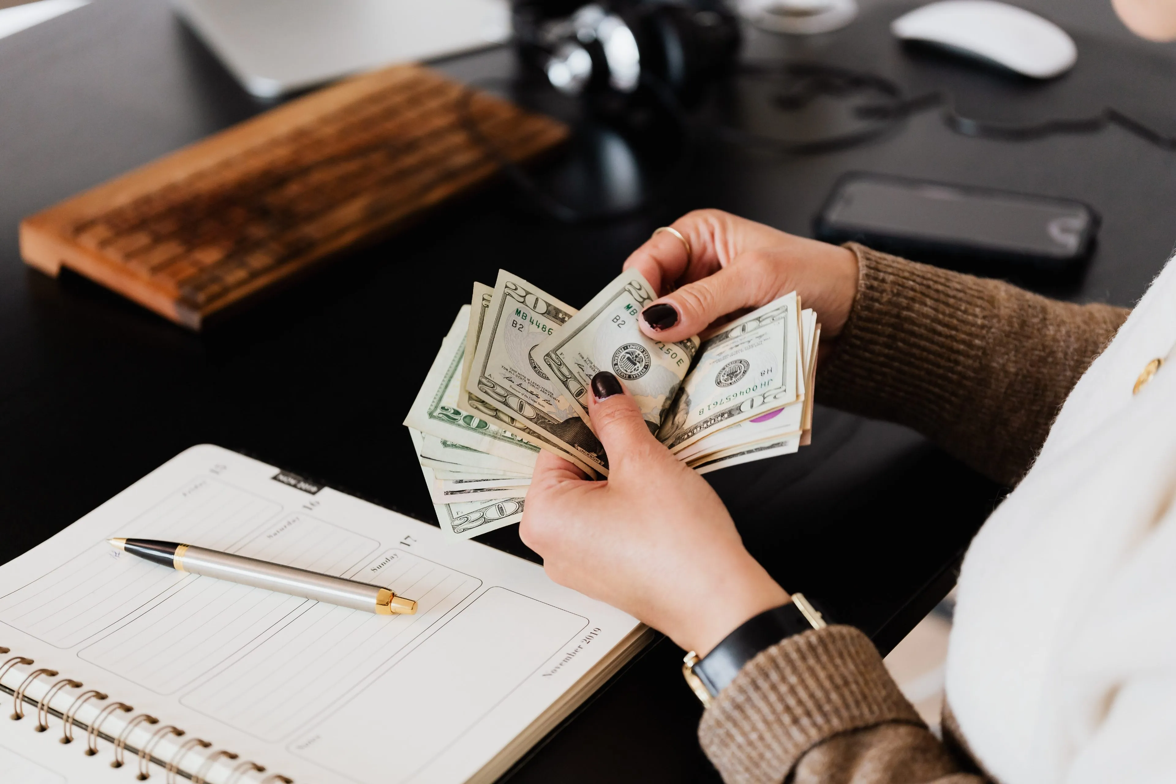 Hands counting money at a desk with a planner open