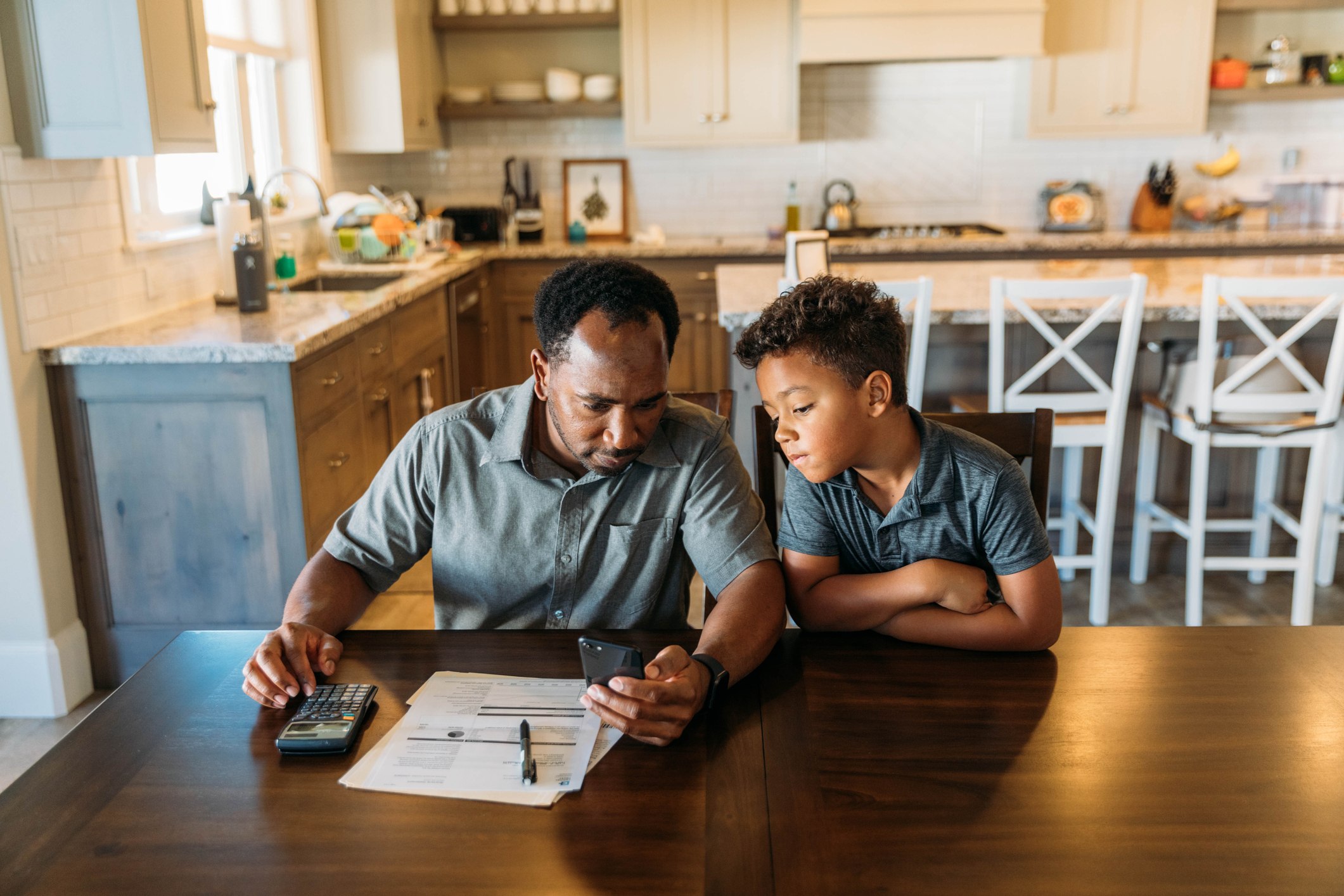 A middle-aged man sits at his dining room table with his young son teaching him about finances