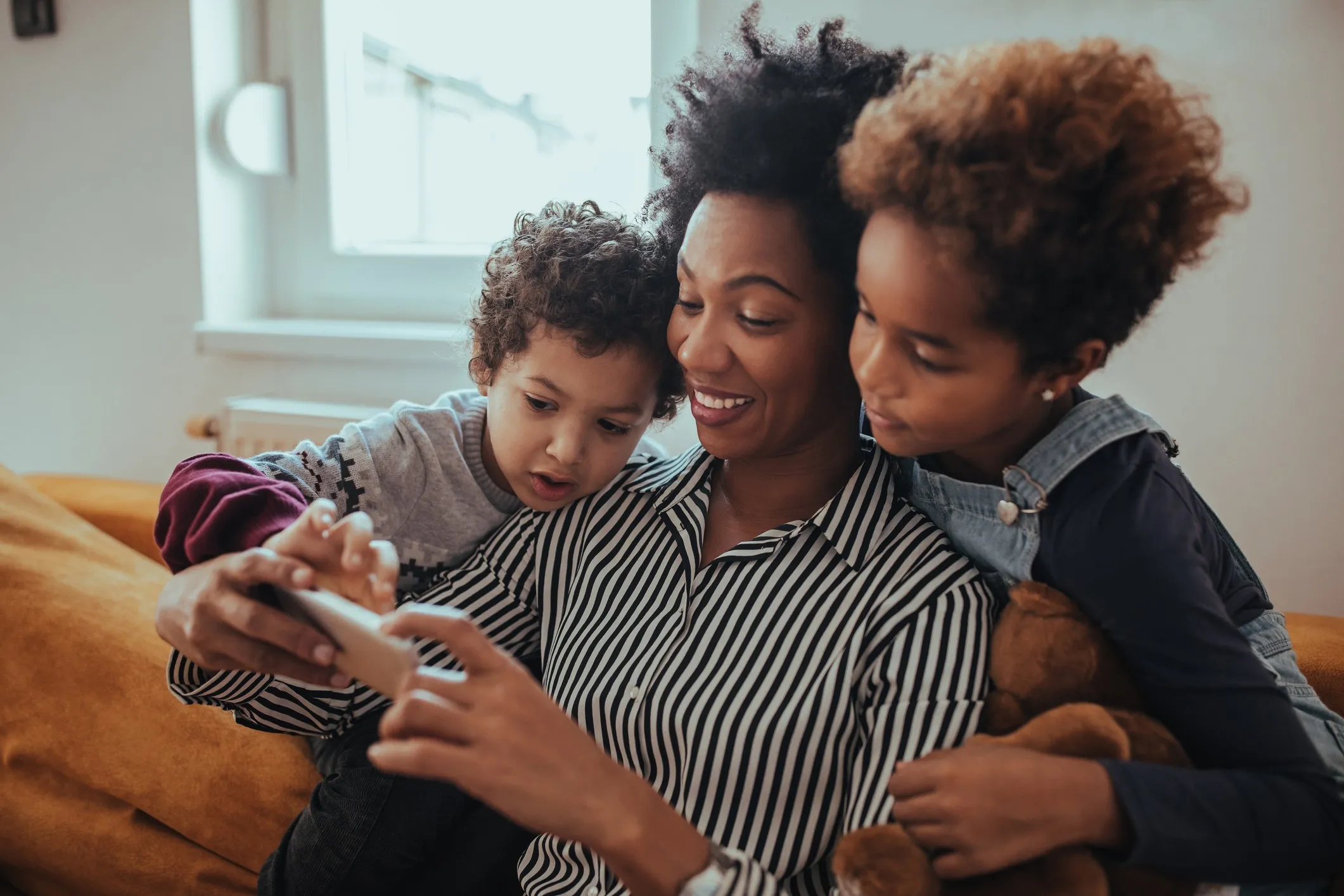 Shot of a mother looking at something on a mobile phone with her children