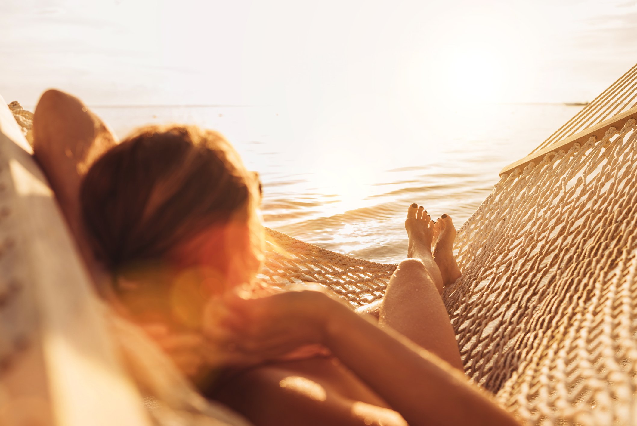 Young woman relaxing in wicker hammock on the sandy beach on Mauritius coast and enjoying sunset light over Indian ocean waves