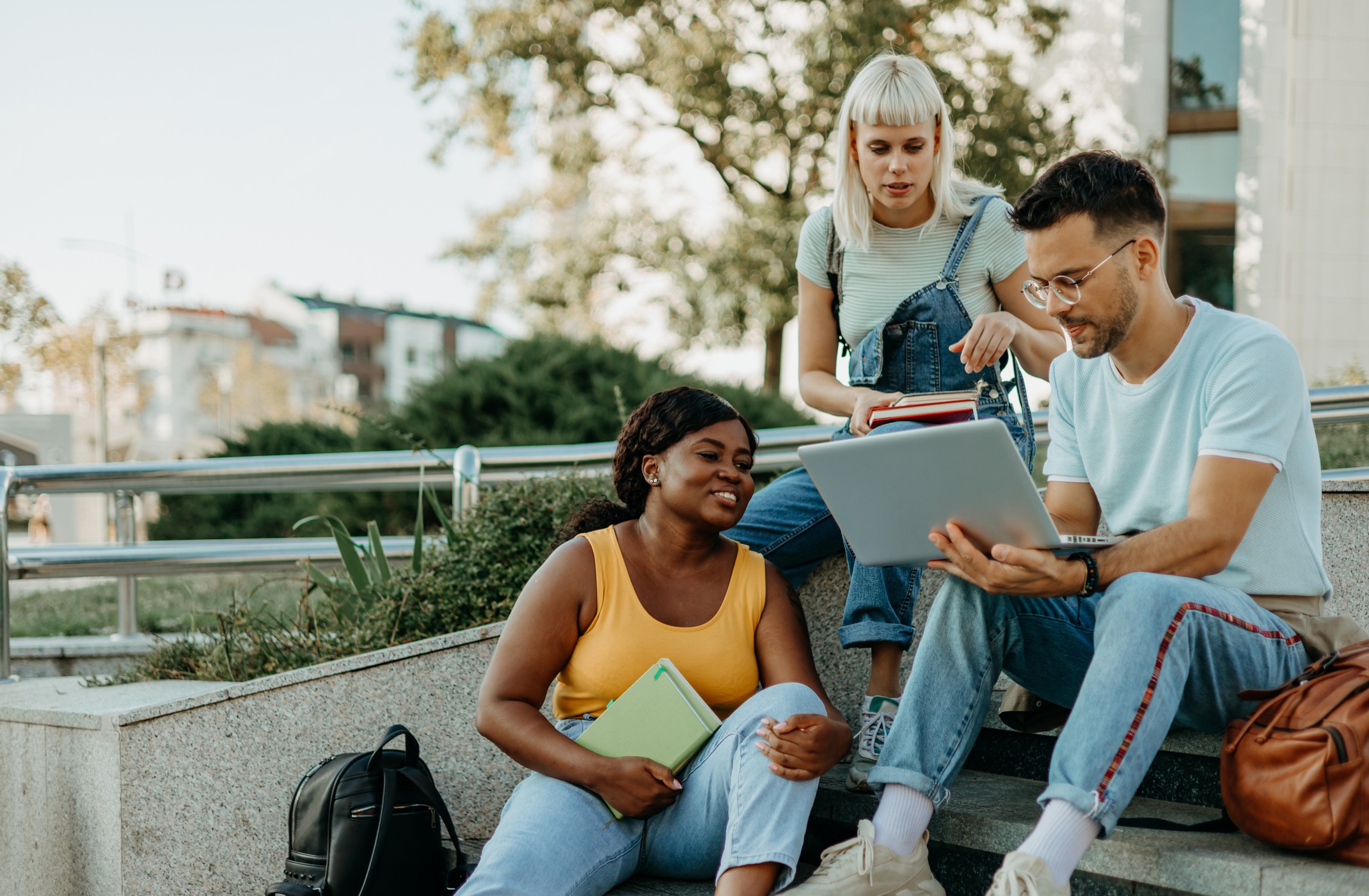Three multiracial college students are sitting outside and working on a group project together.
